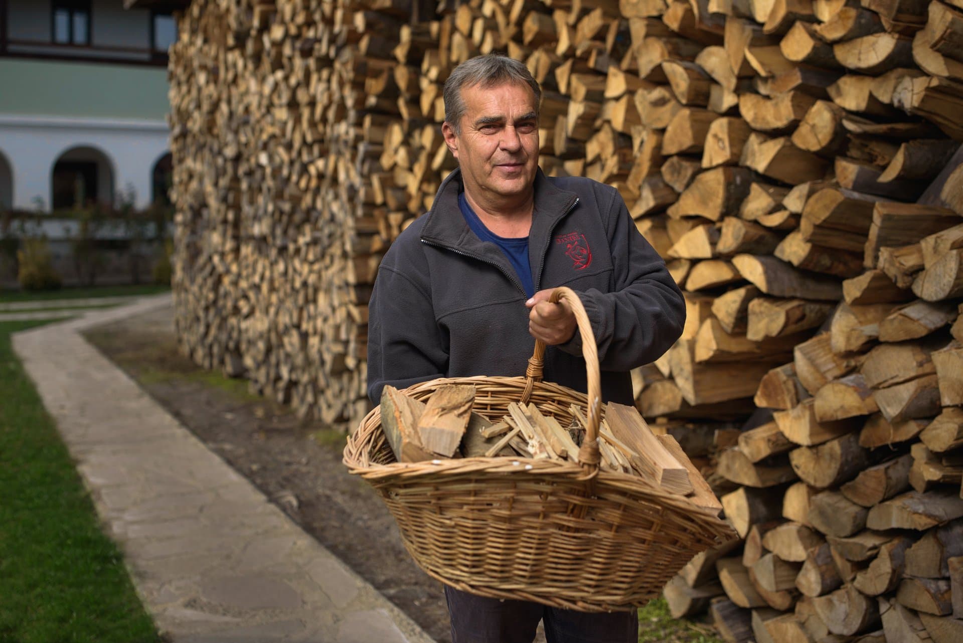 Maintenance Team member carrying a basket of firewood past the castle's wood store